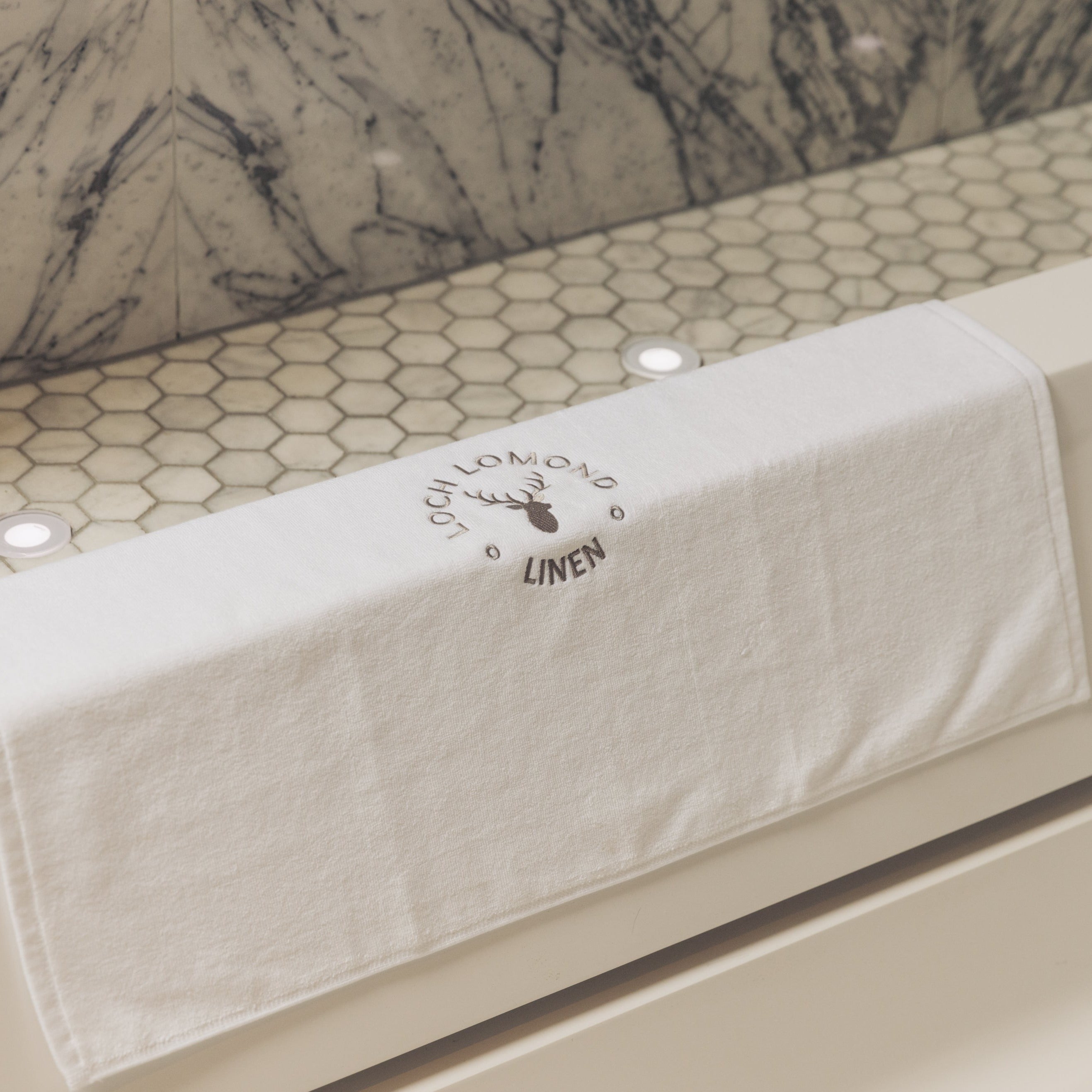 Pure cotton bath mat in white is shown at the edge of a bath tub ready to be used.