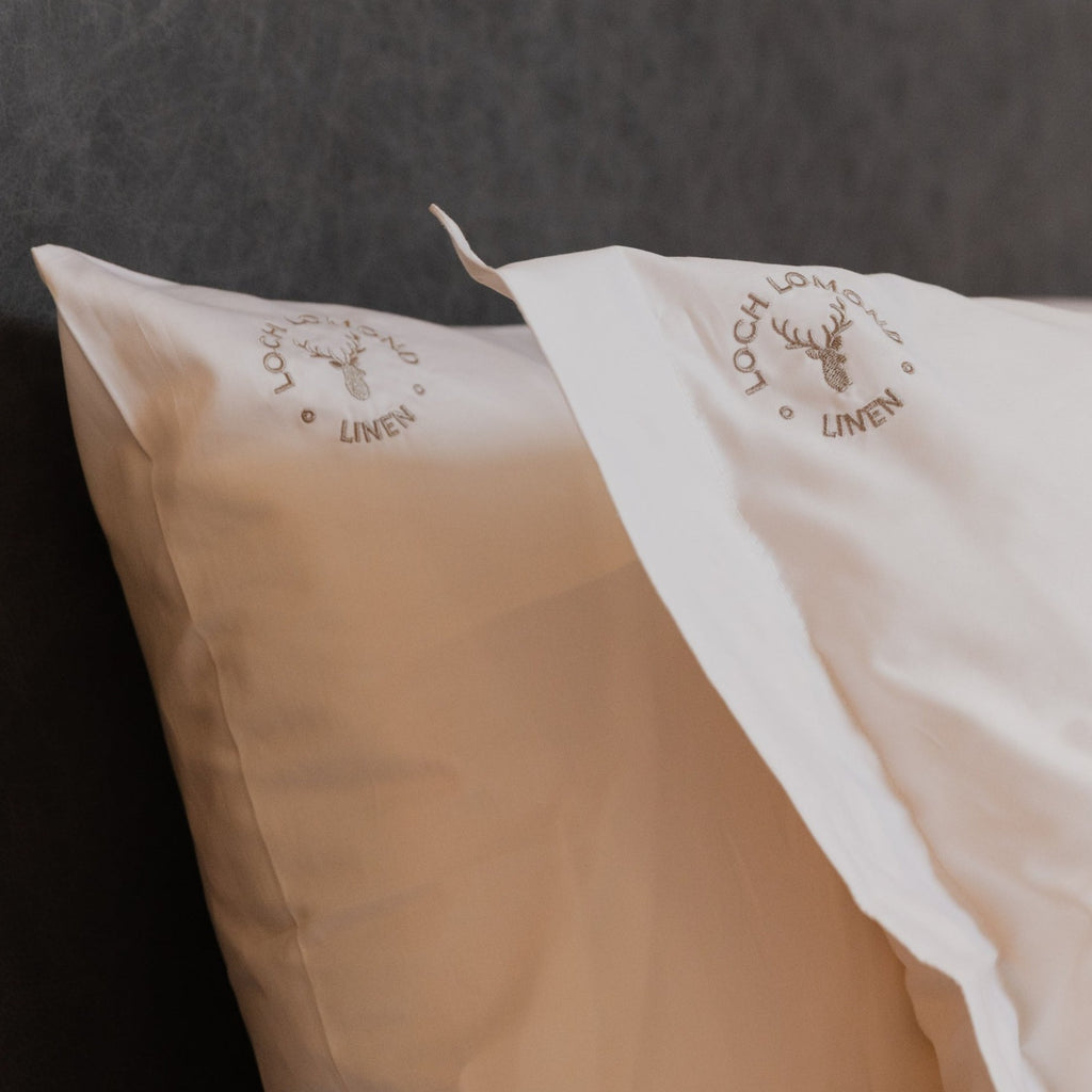 A macro photo of Loch Lomond Linen's logo embroidered in the corner of the luxuriously soft white cotton Oxford and Housewife pillowcases.