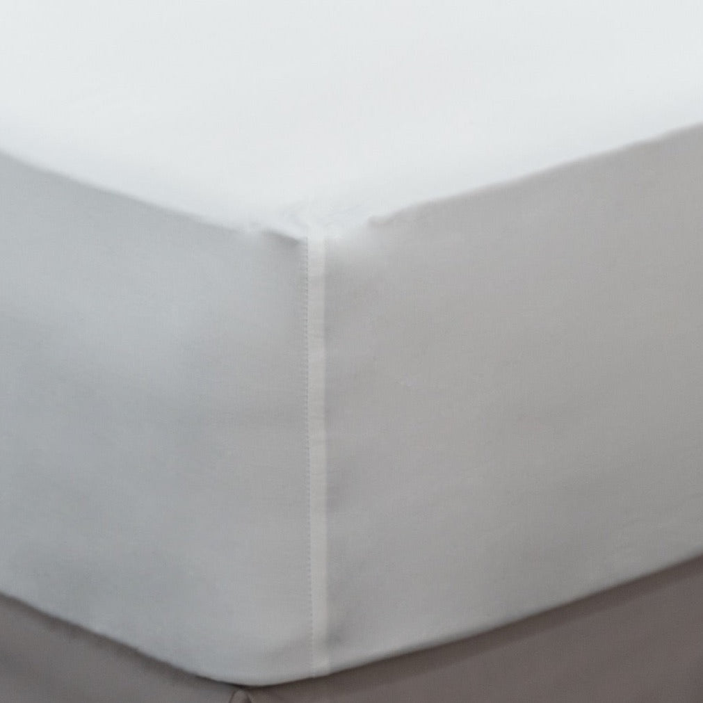 Loch Lomond Linen's white fitted bed sheet is shown on a mattress. Thanks to its elastic corners, the sheet cradles the mattress like a glove.