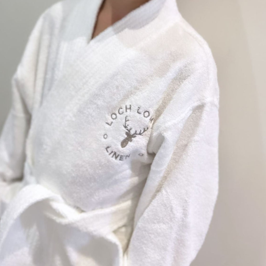 A kid is wearing Loch Lomond Linen's kids robe. The brand's logo is embroidered on the front. The dressing gown is suitable for boys and girls alike.