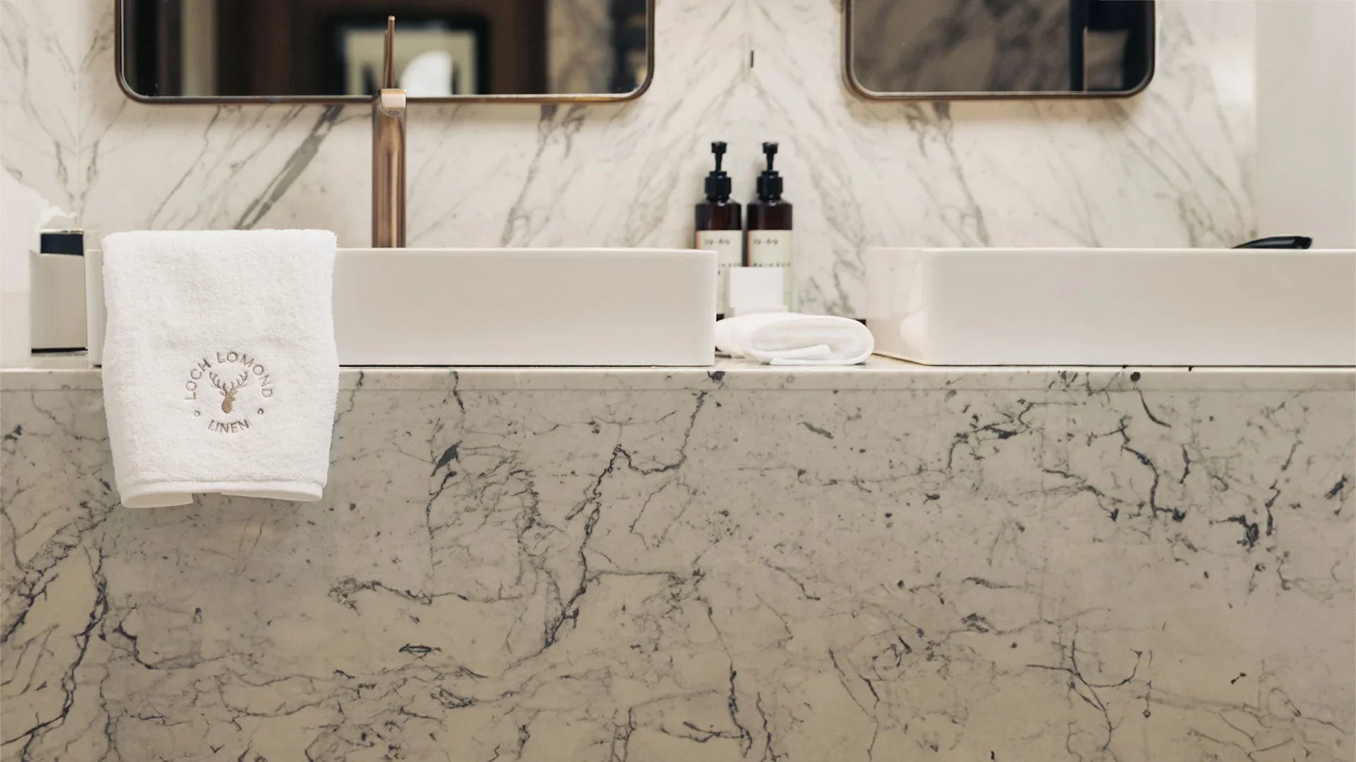 Loch Lomond Linen hotel quality bedding, towel and bathrobe products are shown in a sophisticated bathroom with marble walls.