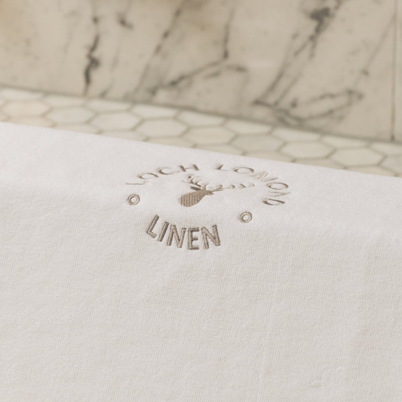 A close photo of Loch Lomond Linen's elegant grey logo embroidered on the white cotton mat.