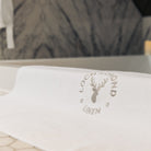 A luxury white cotton bath mat is shown with Loch Lomond Linen's grey logo embroidered in the middle.