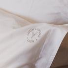 A macro photo of Loch Lomond Linen's logo embroidered in the corner of the luxuriously soft white cotton Oxford pillowcases.
