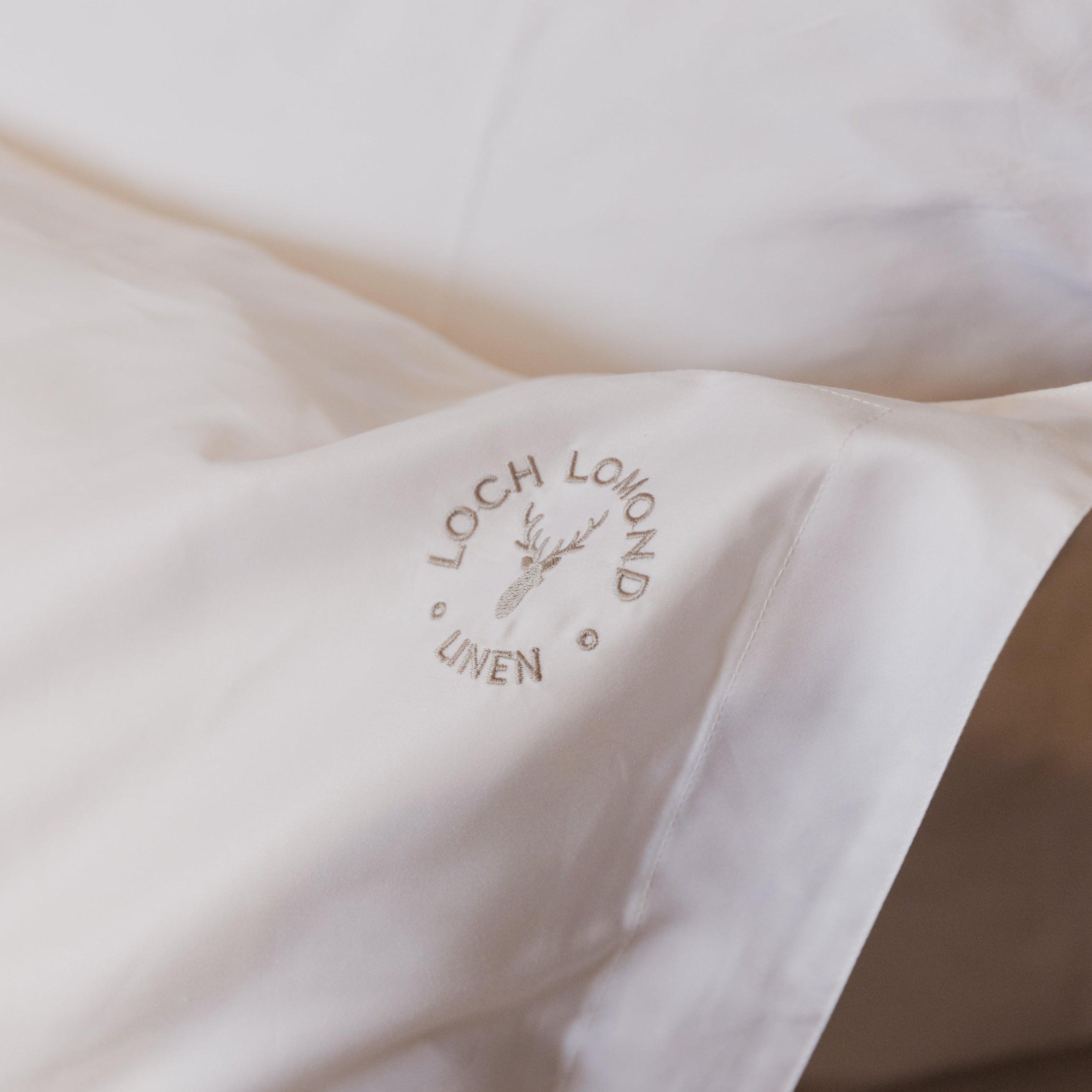 A macro photo of Loch Lomond Linen's logo embroidered in the corner of the luxuriously soft white cotton Oxford pillowcases.