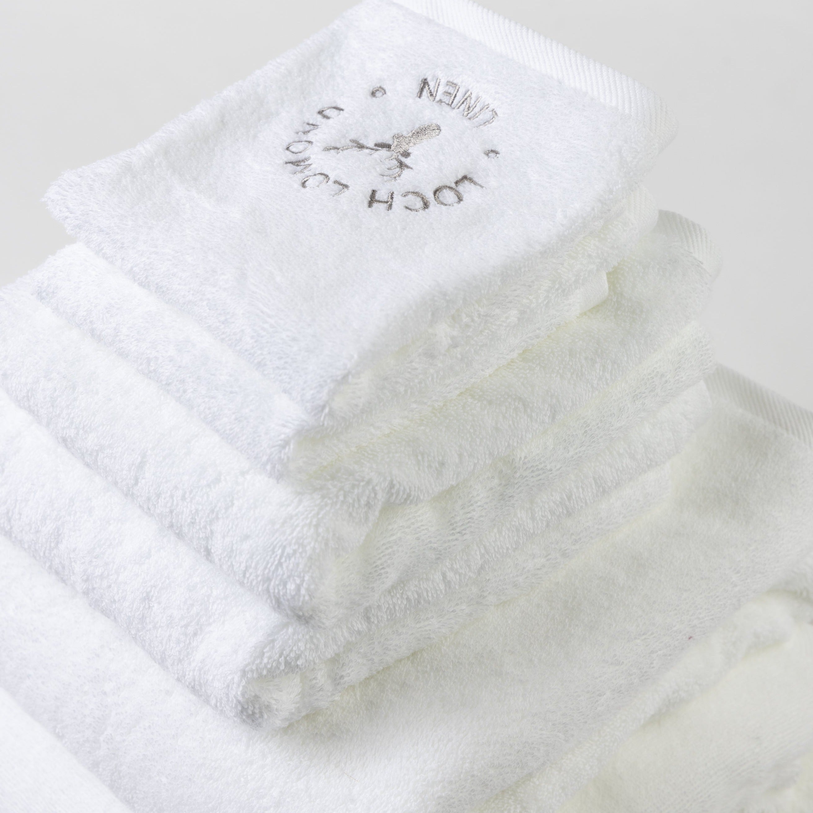Two bath towels, two hand towels and two face towels are folded into a tower and photographed from the top. The grey Loch Lomond Linen logo is elegantly embroidered on the products.