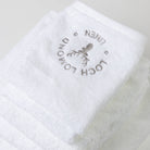 A set of seven luxury 100% cotton white towels are shown withe elegant grey Loch Lomond Linen logo embroidered on the top product.