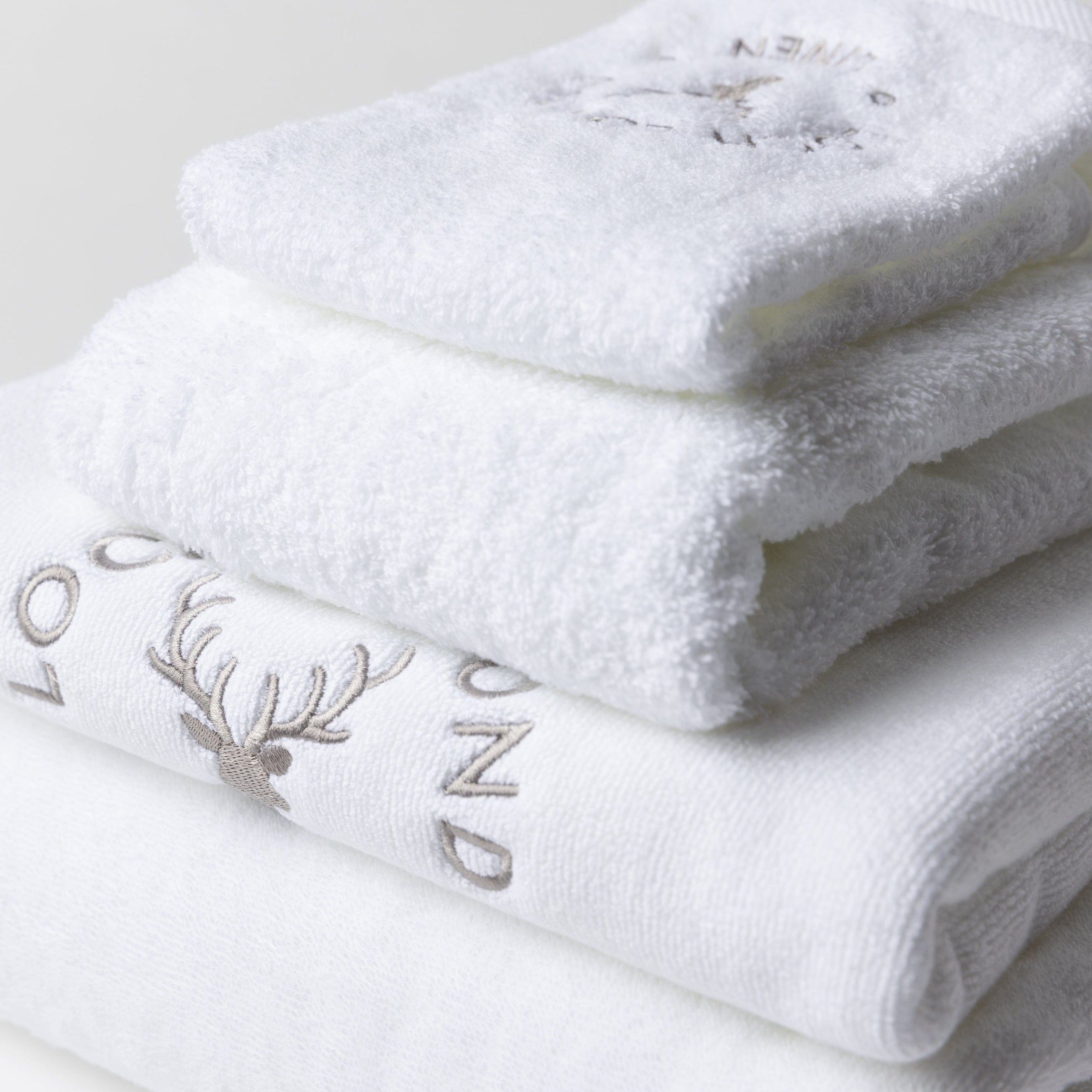 Close photo of the three white cotton towels and bath mat set. The products look very clean and extremely soft. The grey Loch Lomond Linen logo is embroidered onto the products.