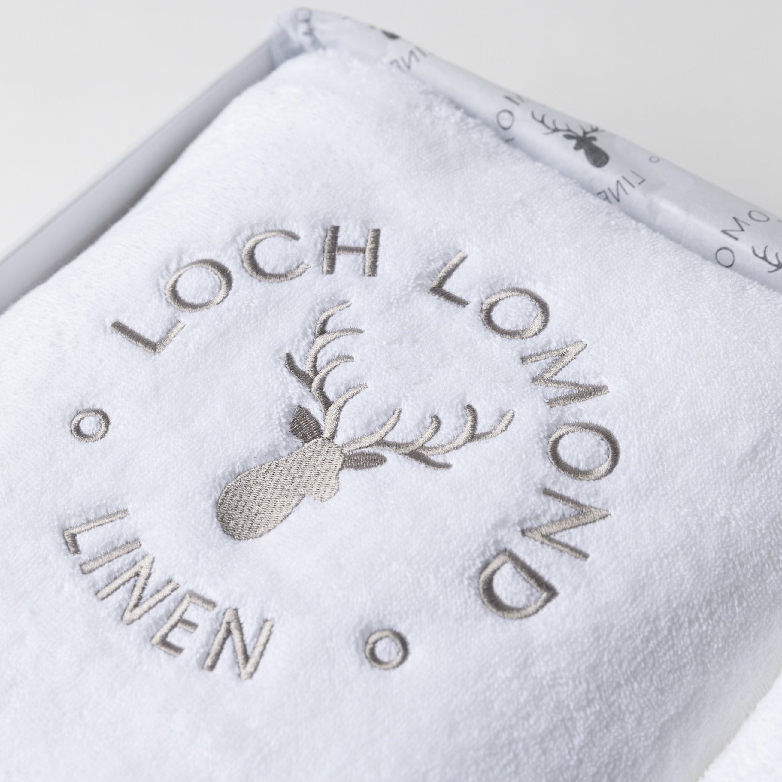Close photo of the grey Loch Lomond Linen logo embroidered on a white 100% cotton towel.