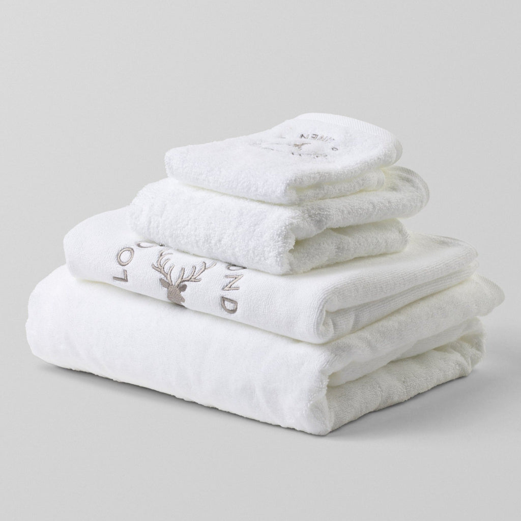 Loch Lomond Linen's three white cotton towels and bath mat set shown neatly folded and placed on top of each other.