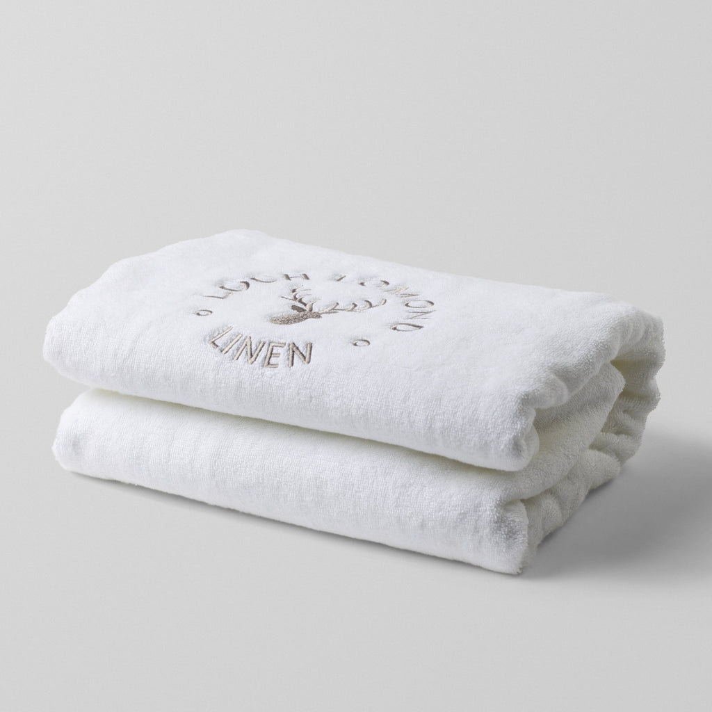 Loch Lomond Linen's white 100% cotton luxury bath towel is photographed on it own. The bath towel is neatly folded with the elegant grey logo showing on the top.