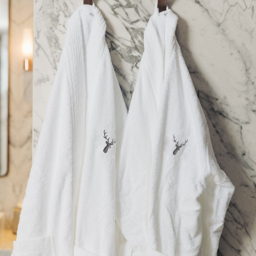 Two white luxurious Loch Lomond Linen bath robes are hanged in a marble bathroom. They are suitable for men and women.