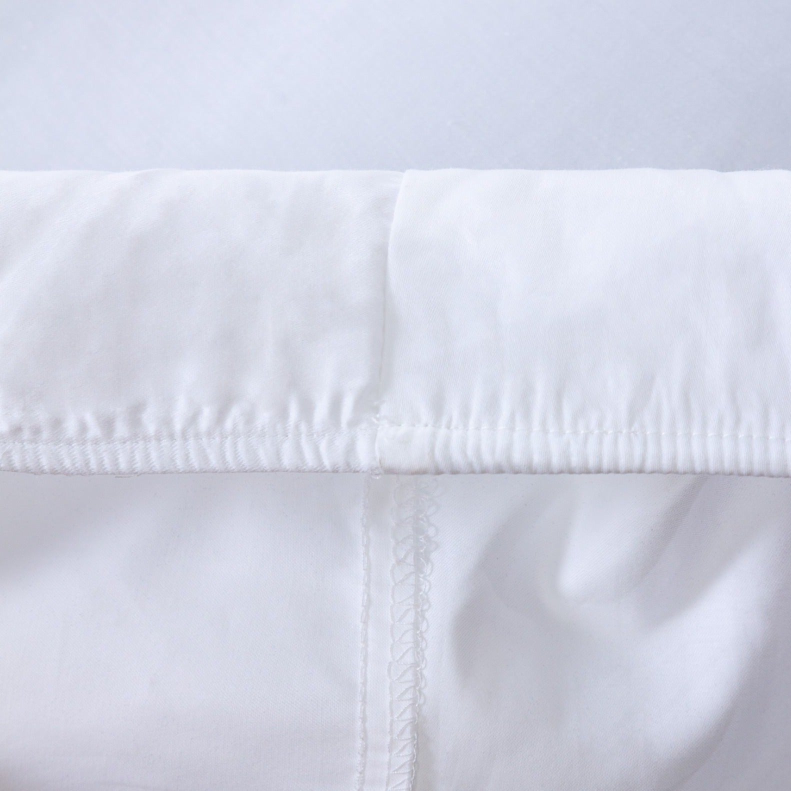 Loch Lomond Linen's white fitted bed sheet's elastic corners are shown in detail. They ensure a snug, tailored fit.